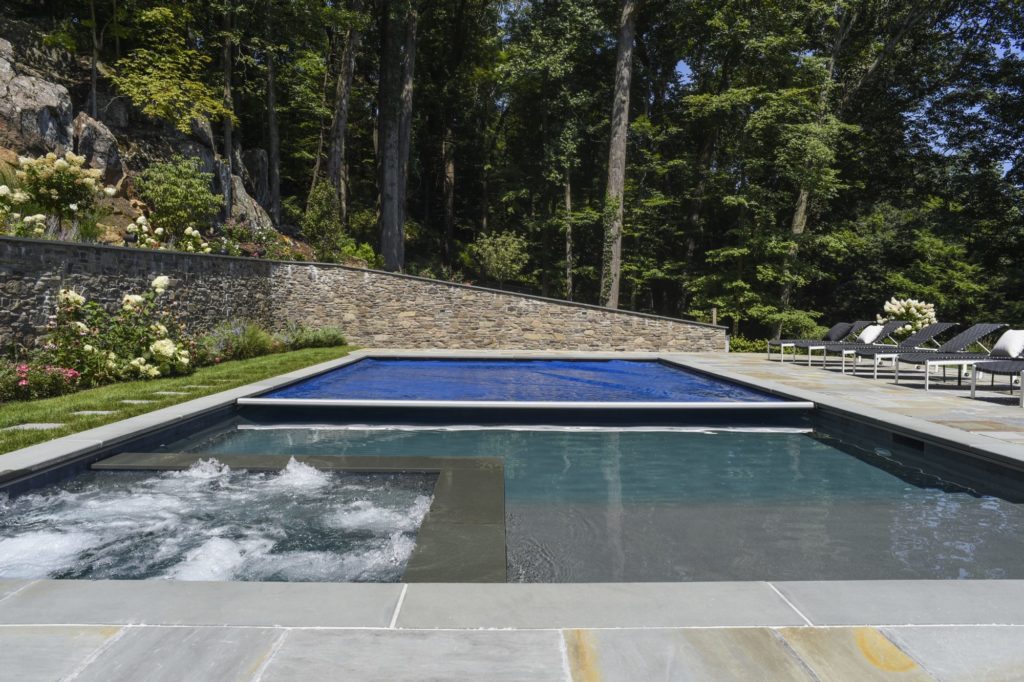 Savings from an automatic pool cover. Royal blue automatic pool cover is halfway covering a large in-ground pool.
